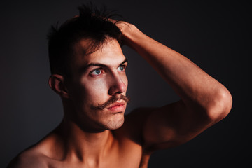 Young shirtless man with mustache thinking by the window