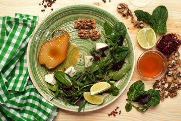 Pear, stewed in honey, mix salad with young spinach, arugula, beet leaves, blue cheese, walnuts on a green plate on a wooden board. Delicious, gourmet salad