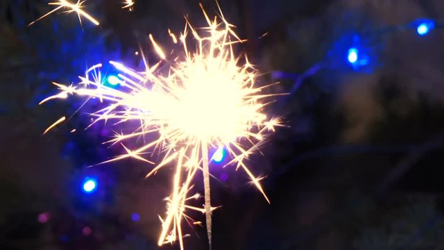 Sparkling firework stick burning in the sark until it extinguishes. colorful lights behind.