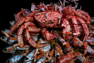 Big hairy boiled crab sits on a heap of dried salted fish on a gift bouquet on the black background. Toned image, close-up