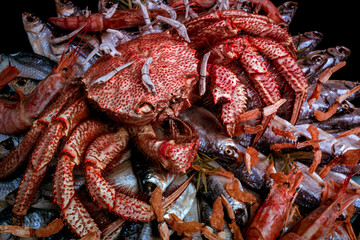 Big hairy boiled crab sits on a heap of dried salted fish on a gift bouquet on the black background. Toned image, close-up