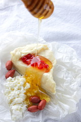 Camembert and cottage cheese on white cloth. Various cheese, peanuts and honey on white background. Cheese, pomegranate grains and nuts. Healthy food
