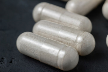 White medical capsules of glucosamine chondroitin, healthy supplement pills on a dark background, macro image