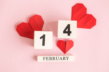 Flat lay of wooden calendar and origami paper hearts against pastel pink background minimal valentines day concept.