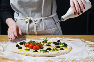 The chef pours olive oil on the raw Focaccia. Top view, wooden background