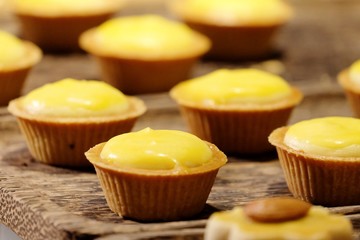 In selective focus a row of lemon cheese tartlets on wooden table with warm light