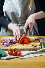 The chef cuts red bell peppers on a wooden chopping Board. Background kitchen, side view