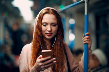 Positive redhead young female with mobile phone in subway train