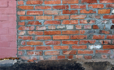 The wall of the house is made of red brick with a cement seam. Part of the wall is painted pink. The Foundation is black, cracked. Background.