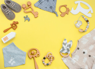 Frame of wooden toys, clothes and shoes on yellow background with copy space