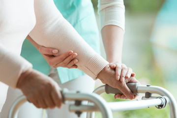 Closeup of elderly lady's hands holding a walker and supporting nurse helping her