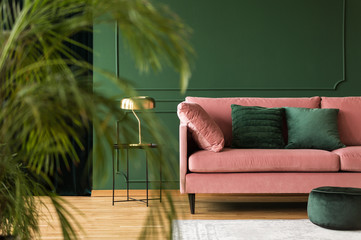 Emerald green pillows on pastel pink couch in stylish living room interior with dark green wall