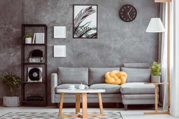 Botanical poster and clock on grey concrete wall in chic living room with industrial black metal...