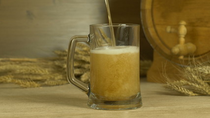 alcohol drink beer pour into a glass against the backdrop of a barrel and a bunch of wheat