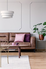 Gold armchair and wooden table in white loft interior with plant and lamp above settee. Real photo