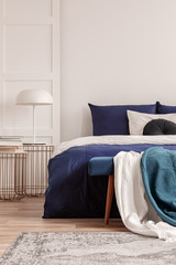 White lamp on stylish golden nightstand table next to king size bed with navy blue bedding