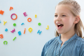Girl on a white background with colorful letters with opened mouth - obrazy, fototapety, plakaty