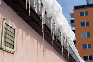 Icicles hanging from roof covered by snow in winter. Slovakia