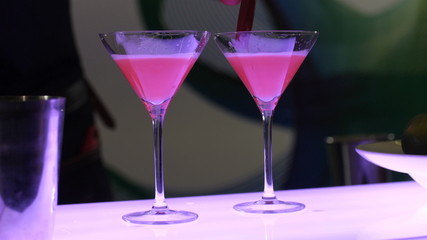 The process of making a cocktail, the bartender in two beautiful glasses on high legs with a prepared drink pours whipped foam from the fruit for decoration and for the special taste of the cocktail