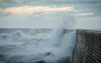 Stormy sea crashing over Tynemouth Pier, Tyneside, Engalnd, UK . In early morning light and sunrise.
