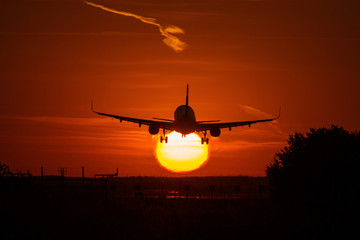 Silhouette of an air plane over the sun with beautiful red clouds in background