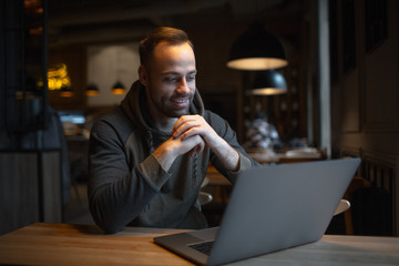 Smiling young man working at laptop in cafe.