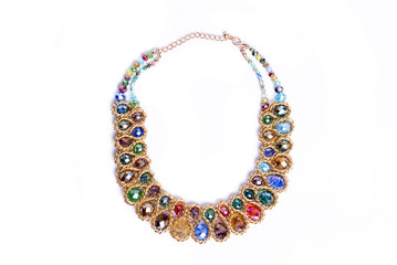 Costume jewelry, factory-produced mass product. Golden look necklace with colored glass gemstones isolated on white background. Top view.Beautiful jewelry with green, red, blue, brown, yellow, purple 