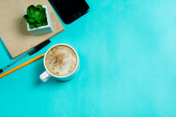 Flat lay, top view office table desk. Workspacewith smartphone, gadget, office supplies, pencil, pen and coffee cup on blue background. Copy space.