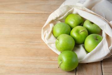 Bio fruit - green apples in white tote canvas fabric. Eco bag cloth shopping sack on wooden background . Zero waste concept. Copy space.