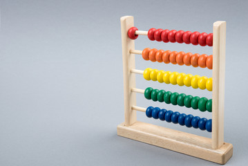 Wooden abacus or abakan. Educational toy for children. Multicolored wooden abacus. Gray background. Place for text. Copy space. Abacus shows  one. First. Close-up.