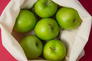 Bio fruit - green apples in white tote canvas fabric. Eco bag cloth shopping sack on colrful red background . Zero waste concept.