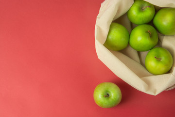 Bio fruit - green apples in white tote canvas fabric. Eco bag cloth shopping sack on colrful red background . Zero waste concept. Copy space.