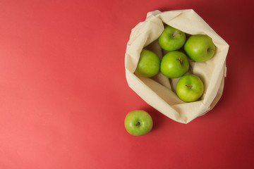 Bio fruit - green apples in white tote canvas fabric. Eco bag cloth shopping sack on colrful red background . Zero waste concept. Copy space.