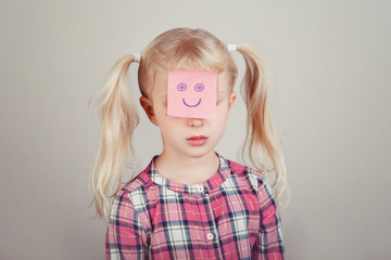 Closeup portrait of sad unhappy white blonde Caucasian preschool girl with funny sticky note paper...
