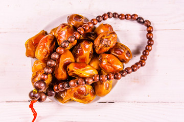 Date fruits and rosary on wooden table. Top view