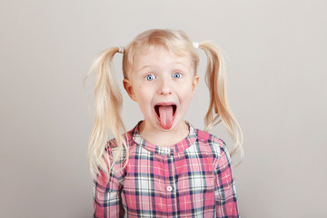 Closeup portrait of funny blonde Caucasian preschool girl making faces in front of camera. Child...