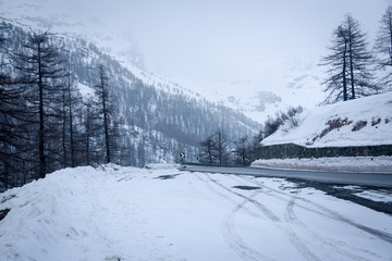   Icy slick curving road covered with snow and snowy trees all around .