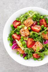 Healthy lunch vegetable salad with baked salmon fish, fresh green peas, lettuce and tomato. Top view