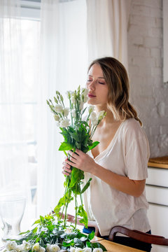 a girl in a white T-shirt is preparing a bouquet of white roses before putting them in a vase on the kitchen table. Lifestyle concept