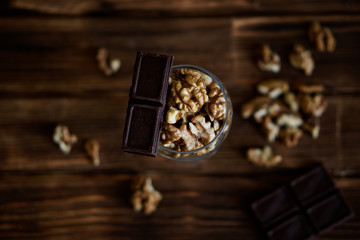 Chocolate slices and peeled walnuts lie on a brown wooden surface. Rustic still life. Healthy food
