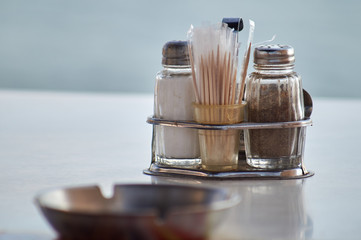 Salt and pepper shakers and a set of toothpicks on a restaurant table, ashtray in the foreground