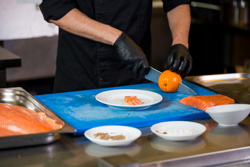 Obraz na płótnie Canvas Theme cooking is a profession of cooking. Close-up of a Caucasian man's hand in a restaurant kitchen preparing red fish fillets salmon meat in black latex gloves uniform
