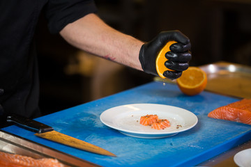 Theme cooking is a profession of cooking. Close-up of a Caucasian man's hand in a restaurant kitchen preparing red fish fillets salmon meat in black latex gloves uniform