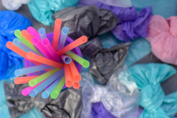 Bright multi-colored plastic tubules in a purple glass on the background of garbage bags