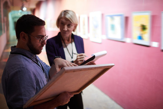 Portrait Of Two Art Gallery Workers Inspecting Paintings In Museum Exhibition, Copy Space