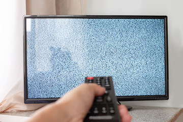 Hand with TV remote control in front of the screen with white noise on it - tuning the television...