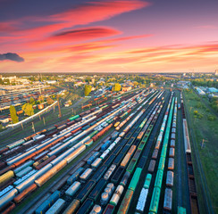 Aerial view of freight trains on railway station at colorful sunset. Wagons with goods on railroad....