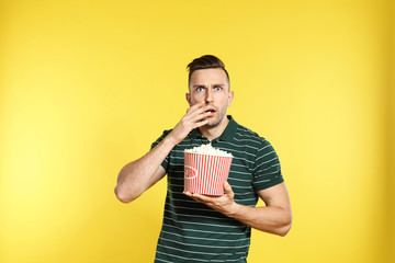 Fototapeta premium Emotional man with popcorn during cinema show on color background