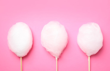 Sticks with yummy cotton candy on color background, top view