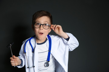 Cute little child in doctor uniform with reflex hammer on black background